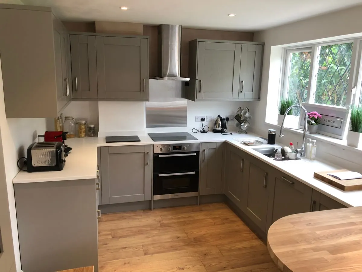 Grey shaker kitchen with white worktops, chimney extractor, integrated oven and oak flooring