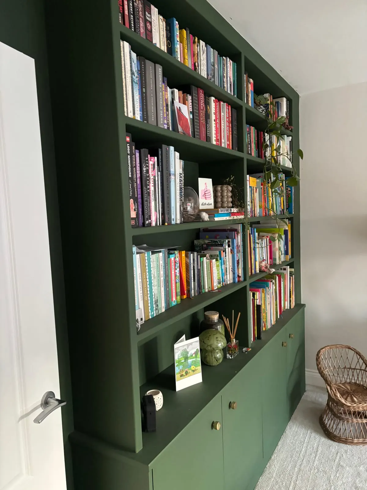 Fitted dark green bookcase with open shelves of books above brass-knobbed cupboard bases