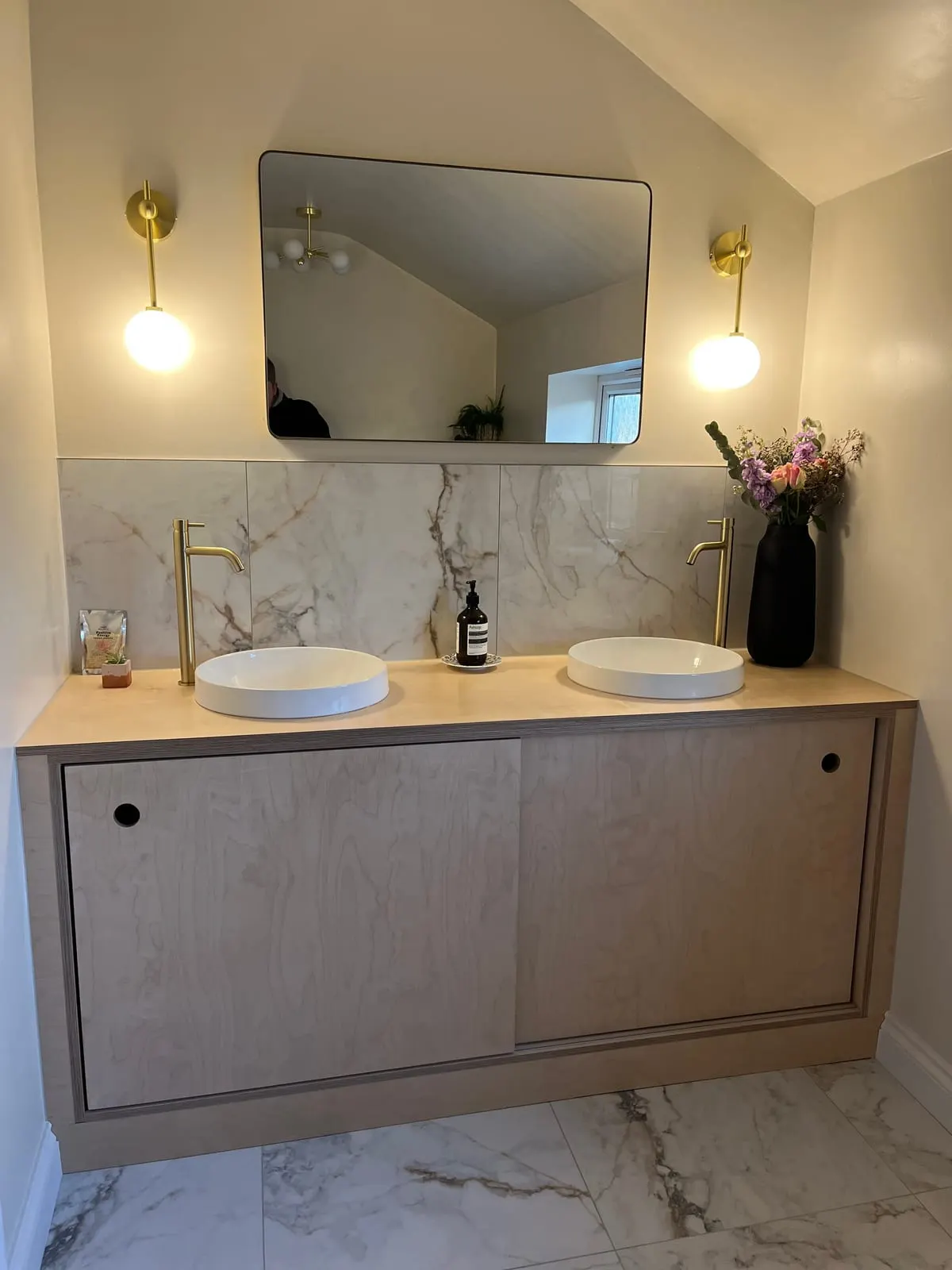 Floating birch ply double vanity unit with twin round basins, brass taps and marble splashback