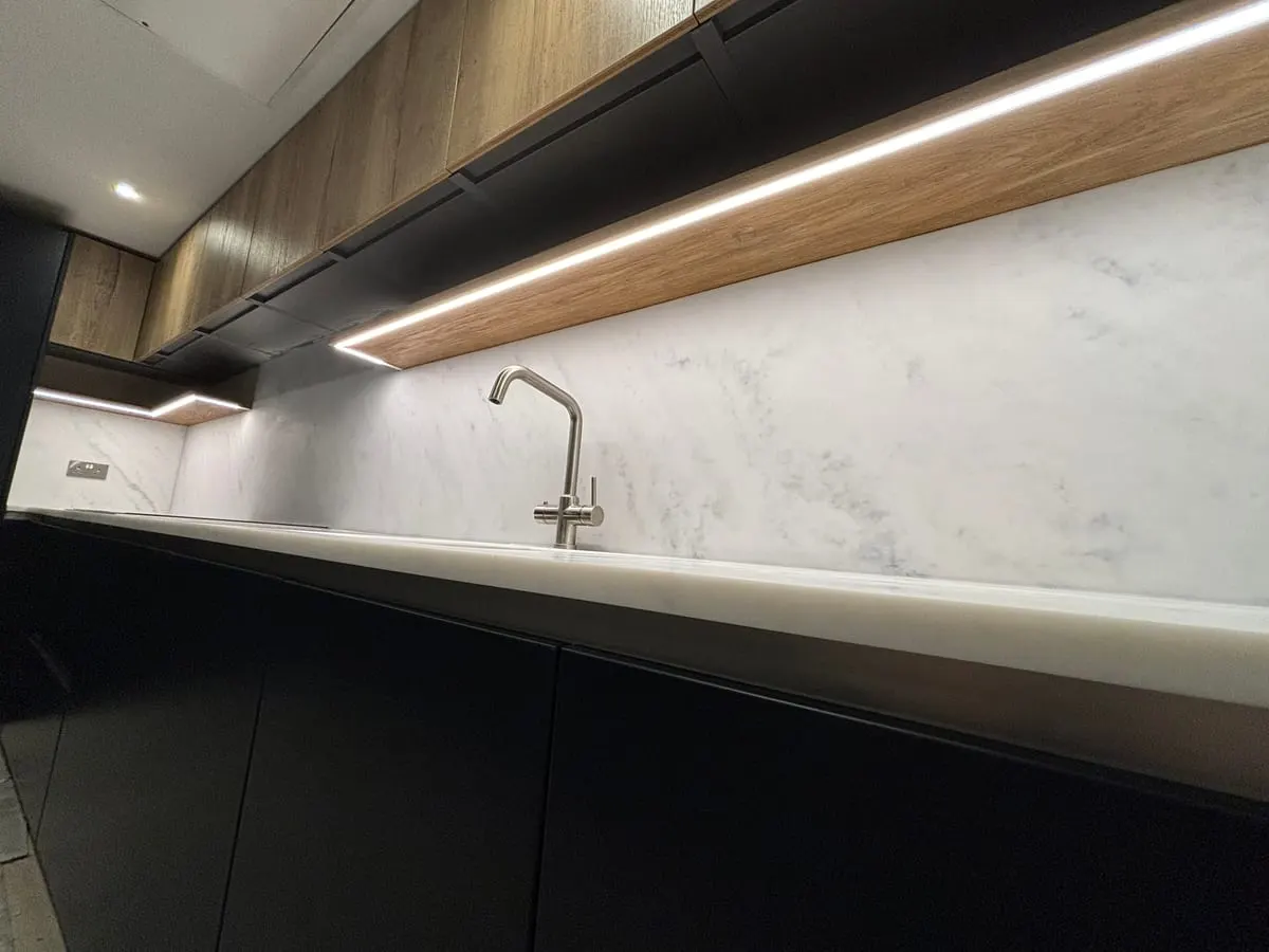 Matt black handleless kitchen units with marble worktop, splashback and LED-lit oak shelf above