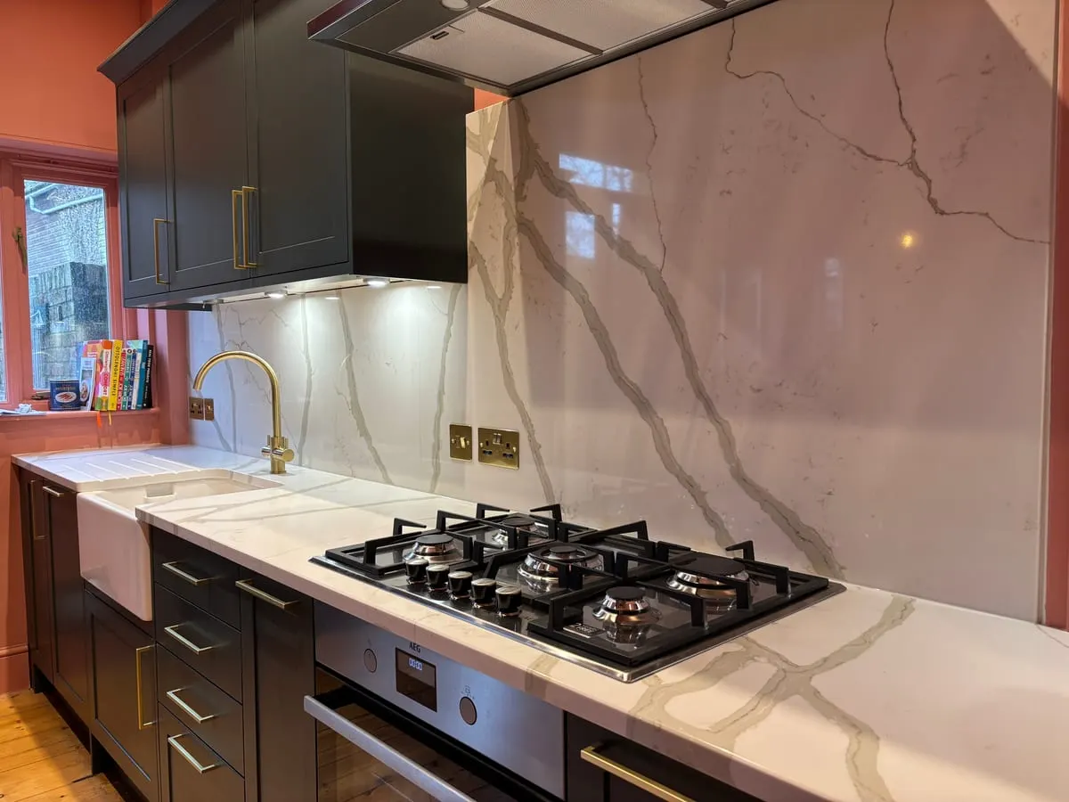 Dark shaker kitchen with veined marble worktop and splashback, gas hob, brass tap and butler sink
