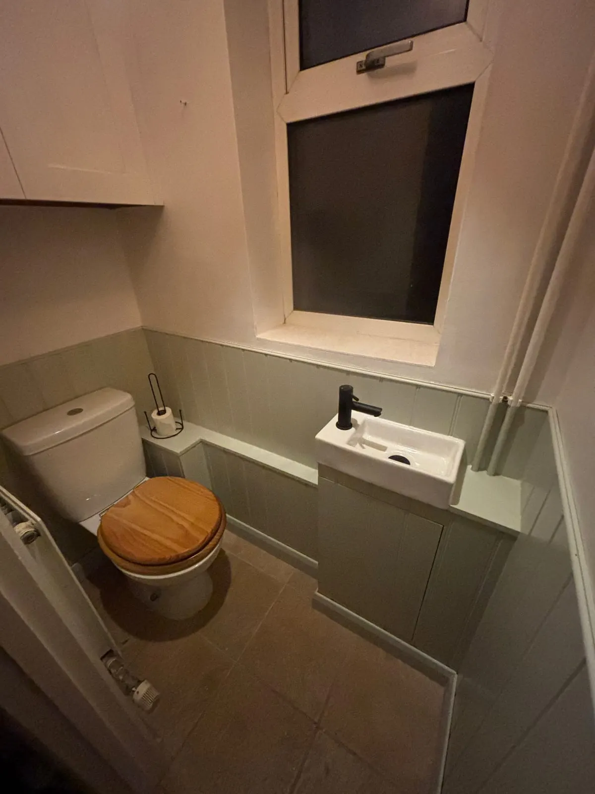 Compact cloakroom with sage green panelling, wooden toilet seat, small basin and tiled floor