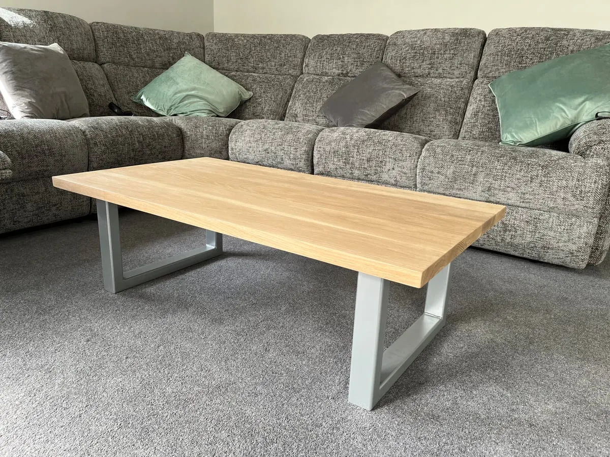 Solid oak coffee table with grey steel loop legs on grey carpet in front of a fabric corner sofa