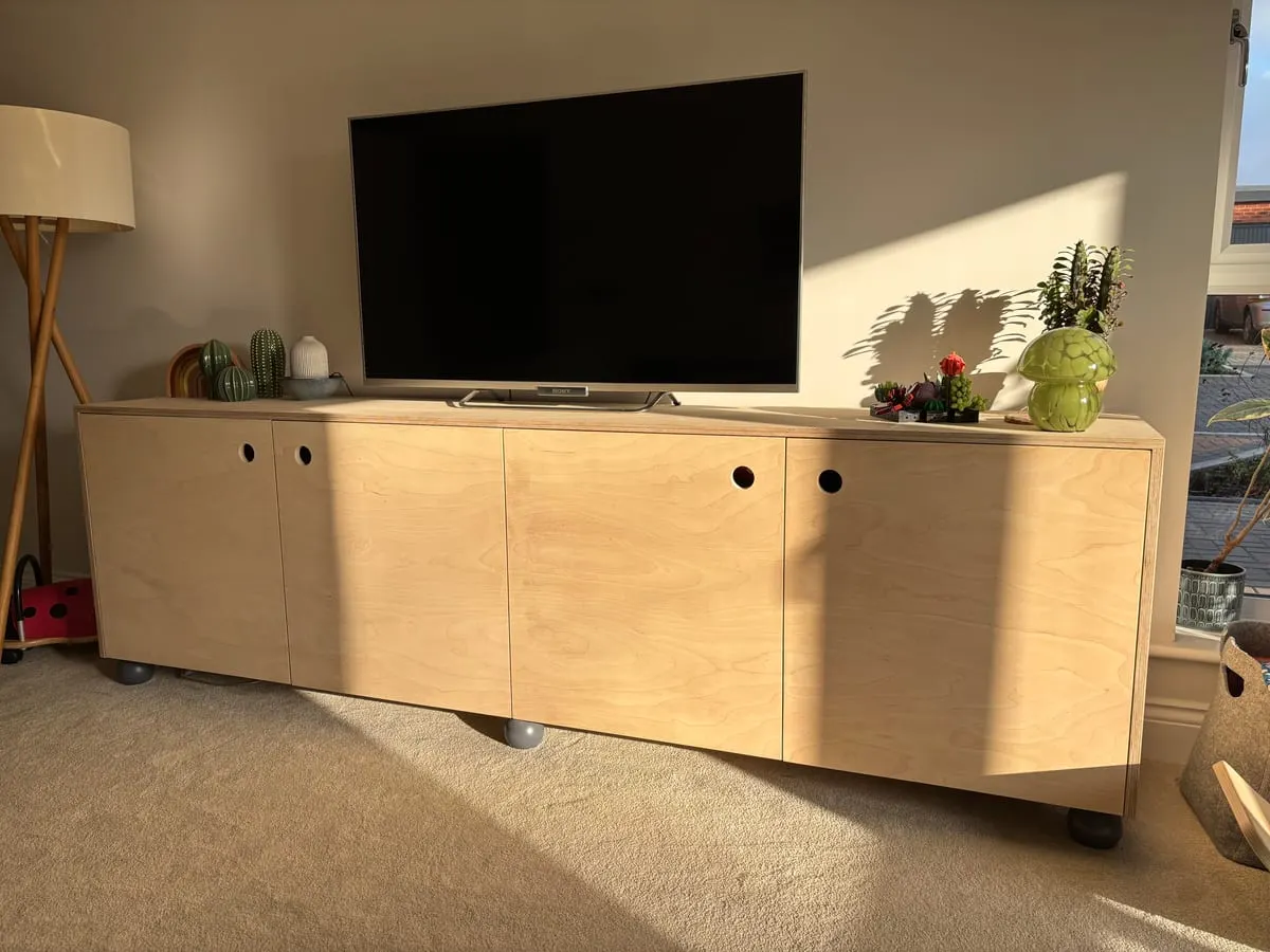 Birch plywood media unit with four sliding doors and cut-out handles supporting a large flat-screen TV