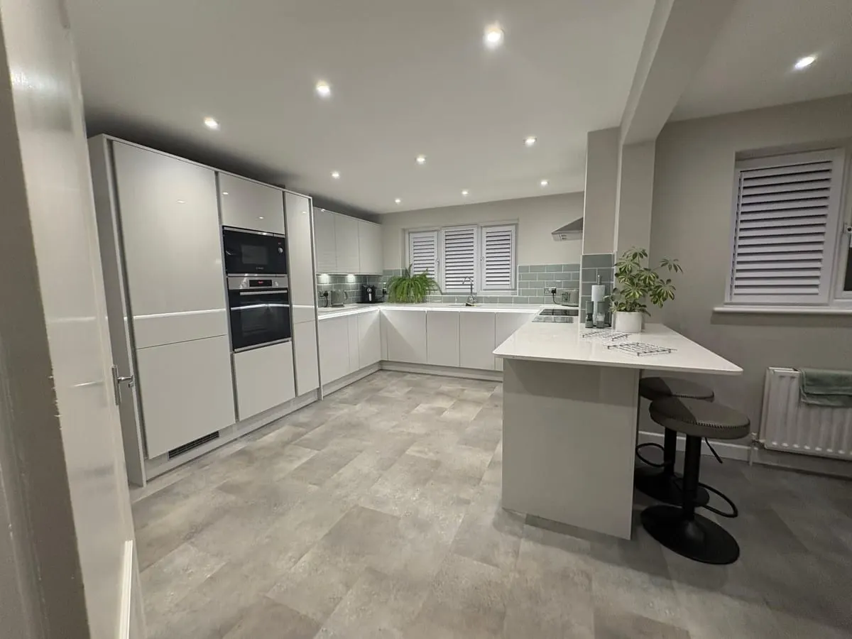 Handleless white kitchen with tall oven housing, peninsula breakfast bar and grey tiled flooring