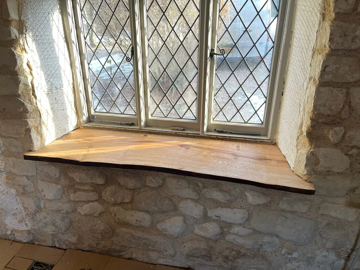 Live-edge solid oak window seat fitted into an exposed stone wall beneath a leaded window