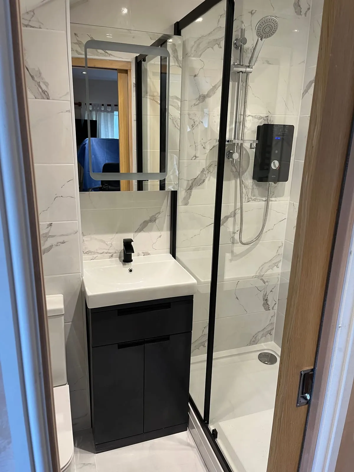 Compact shower room with marble-effect tiling, black framed enclosure and black vanity unit with basin