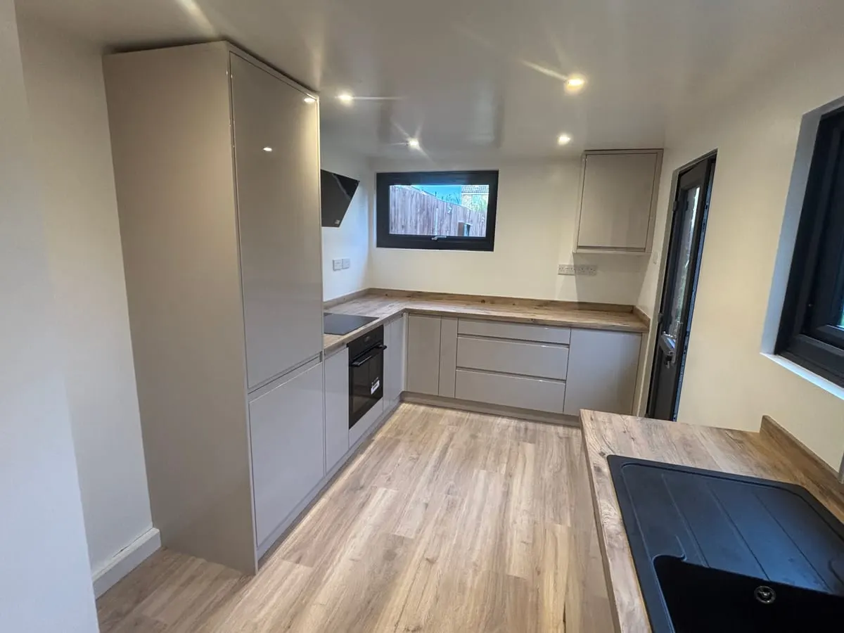 Grey handleless kitchen with oak-effect worktops, built-in oven, hob and wood-effect vinyl flooring