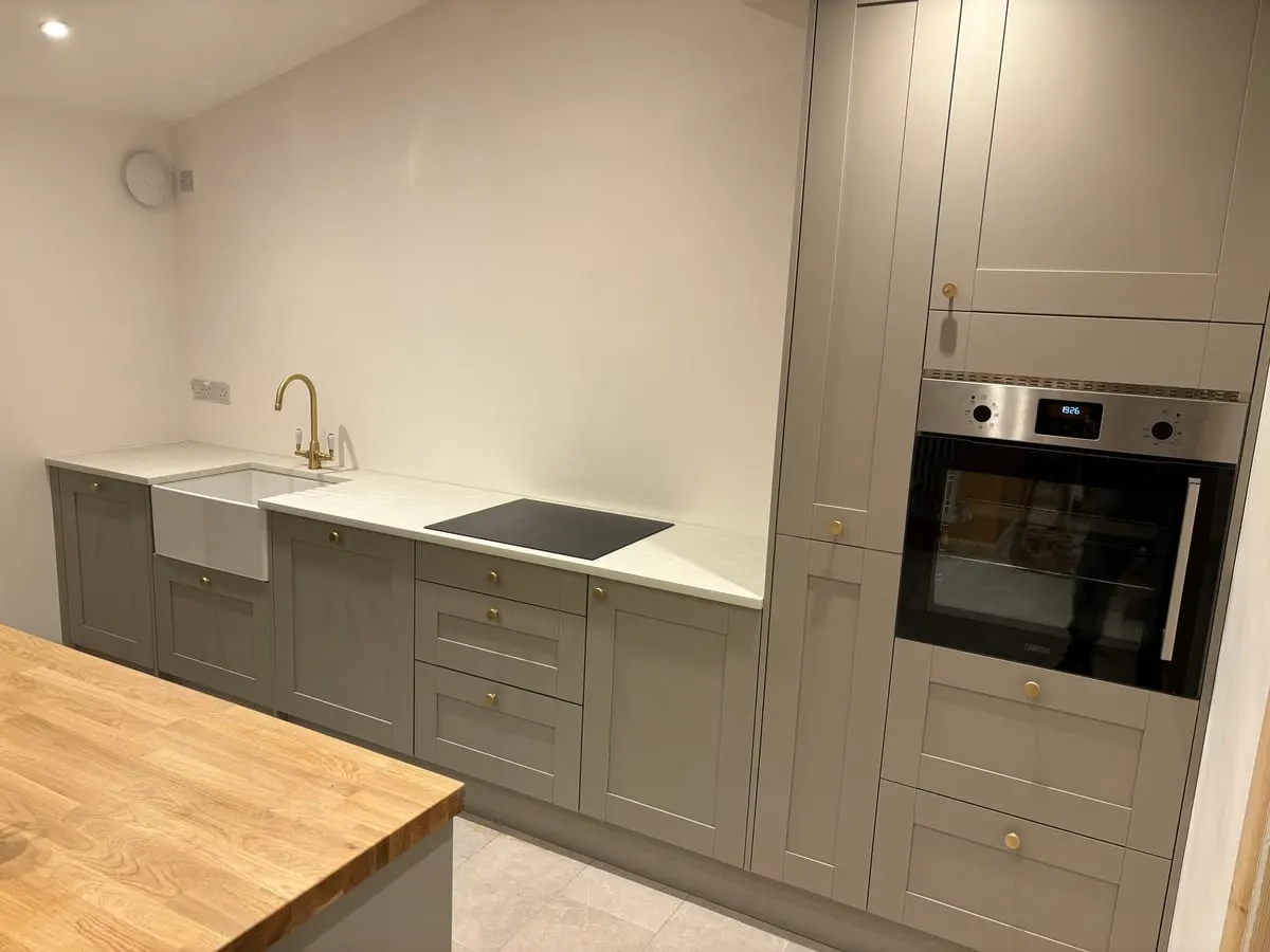 Grey shaker kitchen with Belfast sink, brass tap, induction hob, built-in oven and oak-topped island