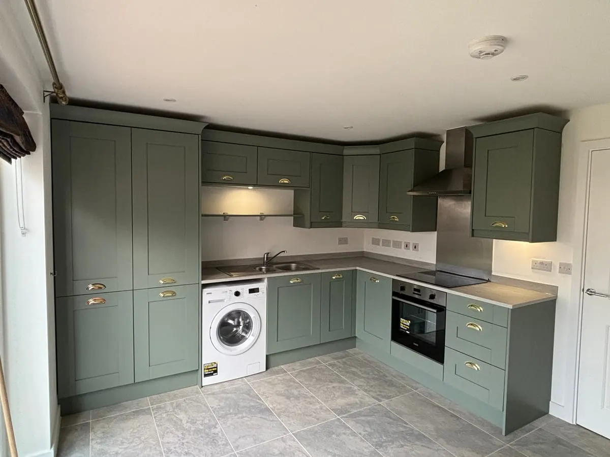 Sage green shaker kitchen with brass cup handles, integrated oven, hob, extractor hood and tiled floor