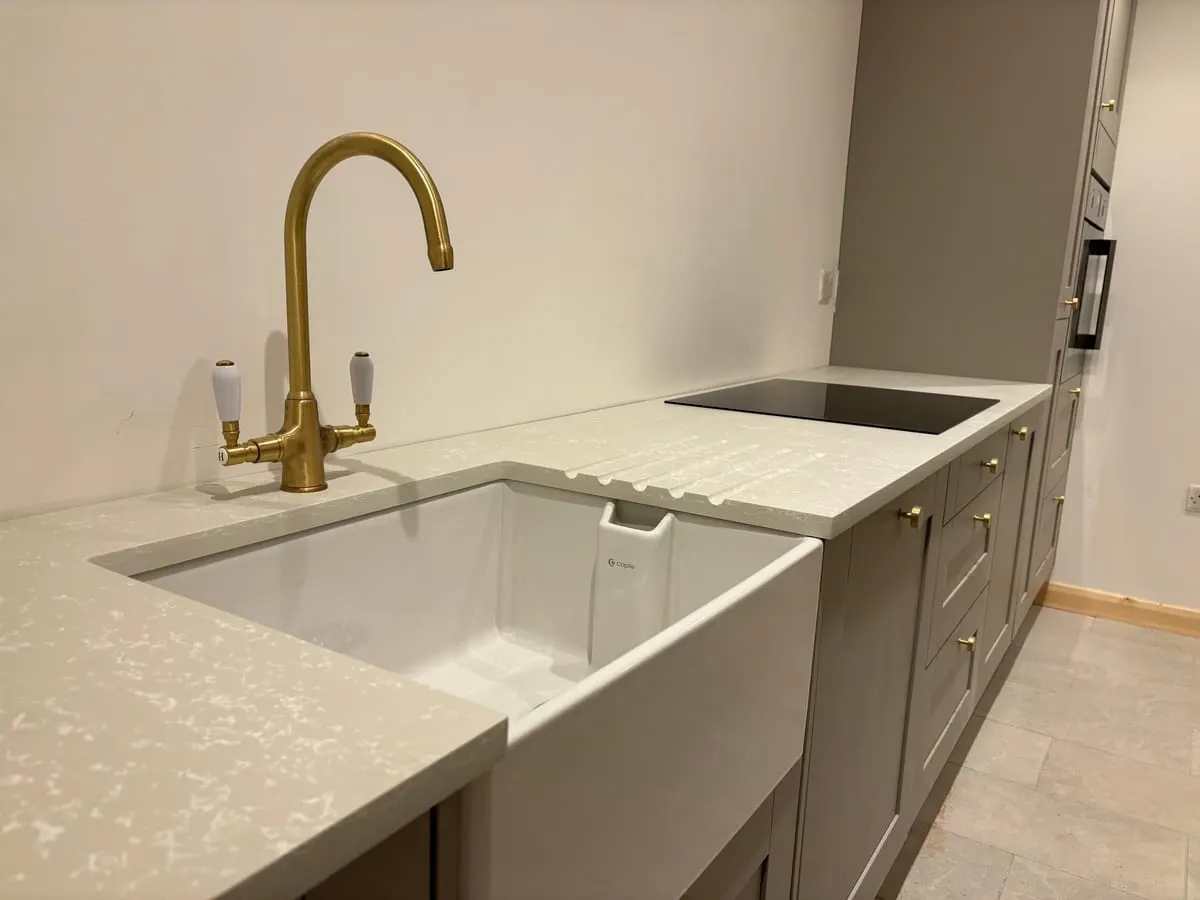 Belfast sink with brass swan-neck tap set into a white quartz worktop beside grey shaker units