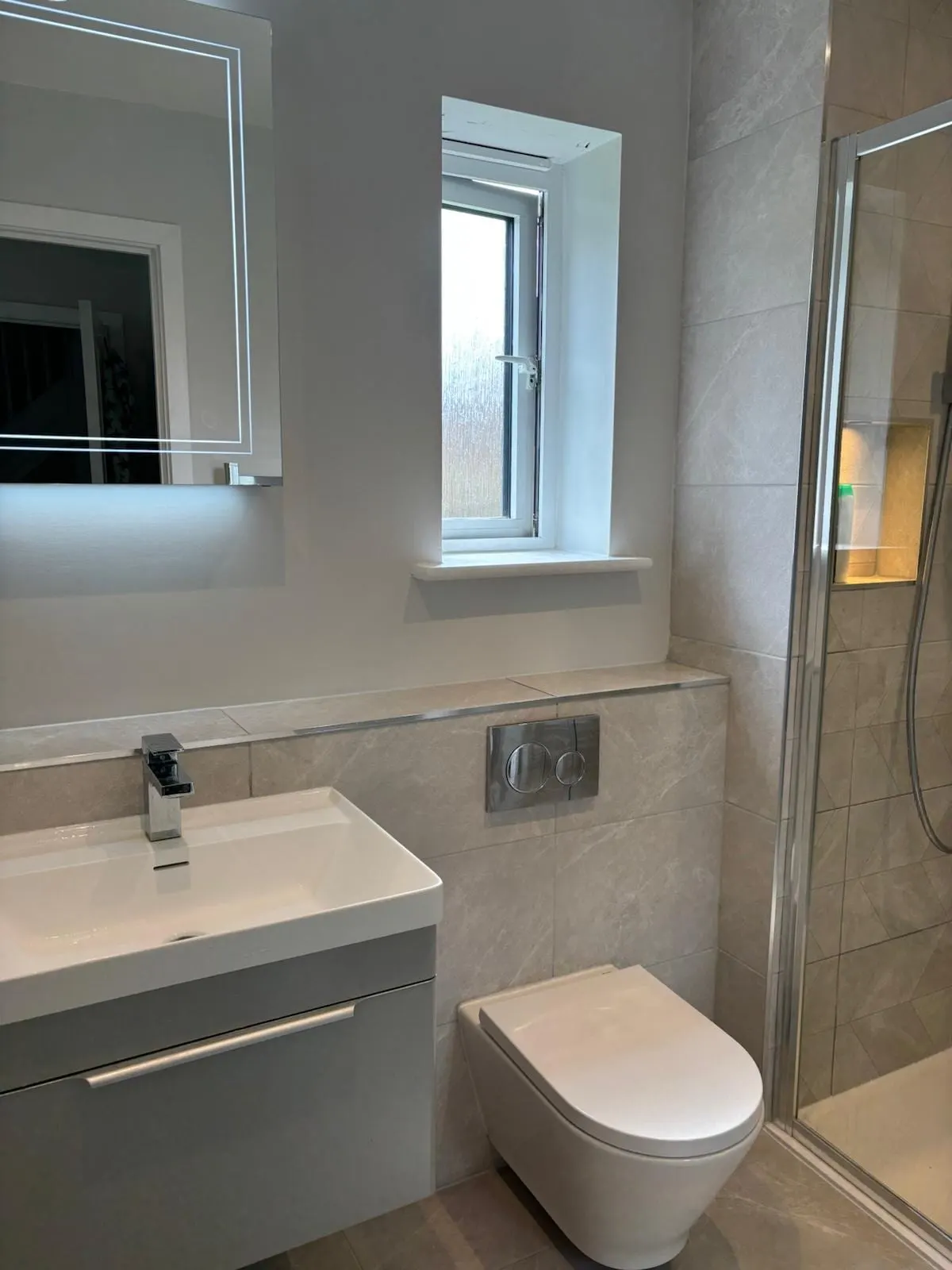 Modern shower room with wall-hung vanity unit, backlit mirror, concealed-cistern WC and glass shower enclosure