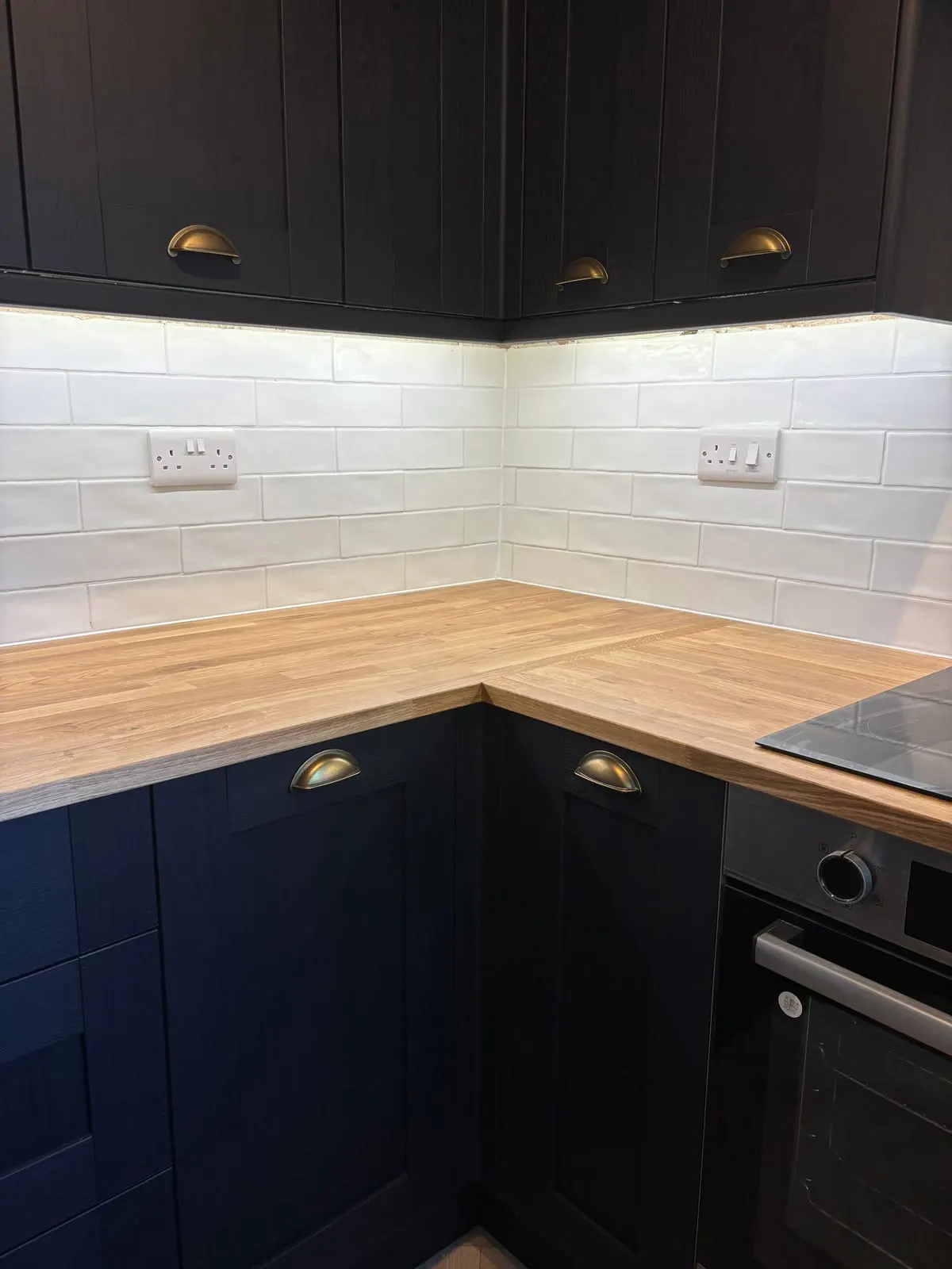 Navy shaker kitchen units with brass cup handles, solid oak worktop and white metro tile splashback