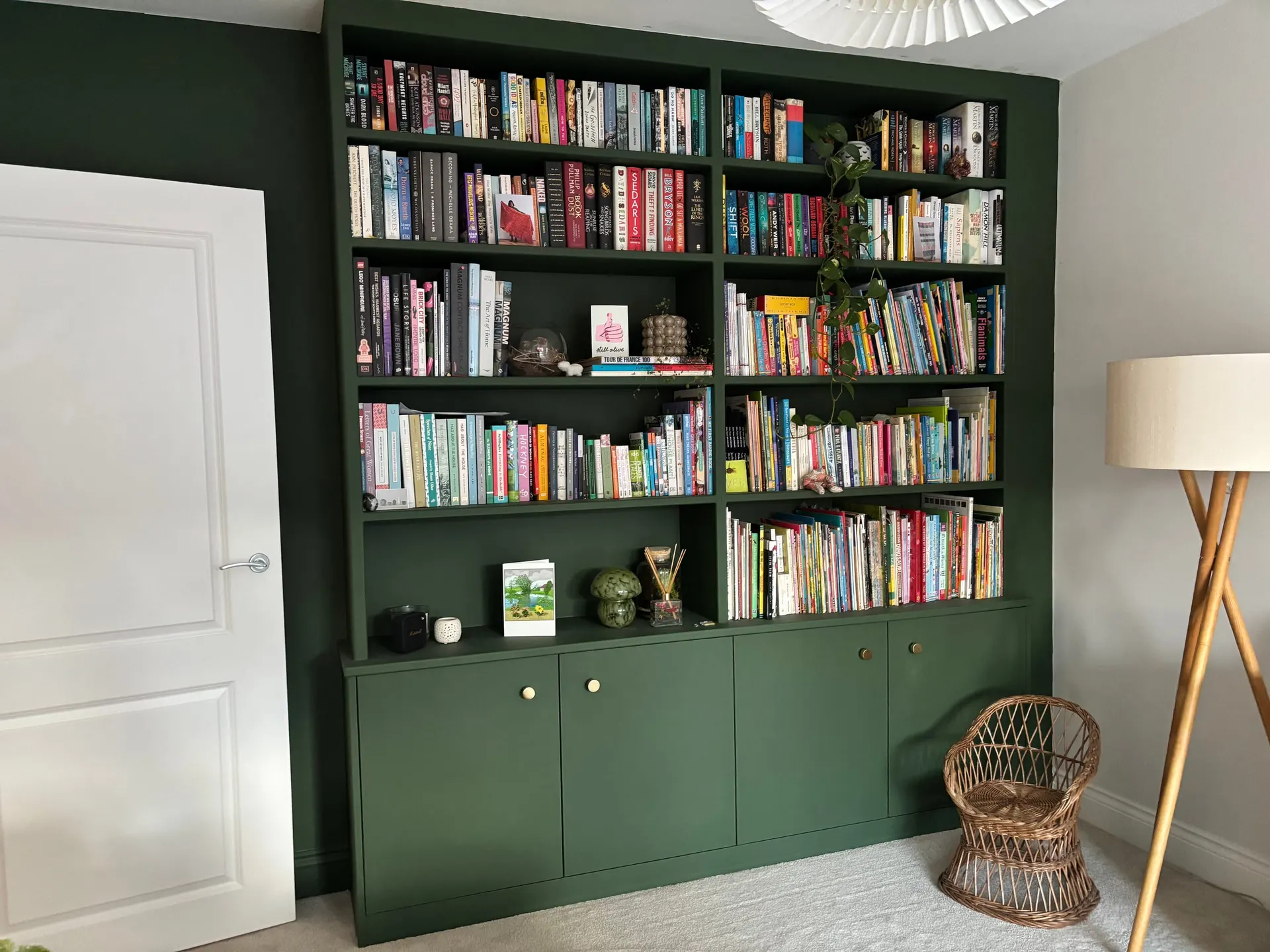 Floor-to-ceiling fitted bookcase painted deep green with brass-knobbed cupboards and shelves full of books