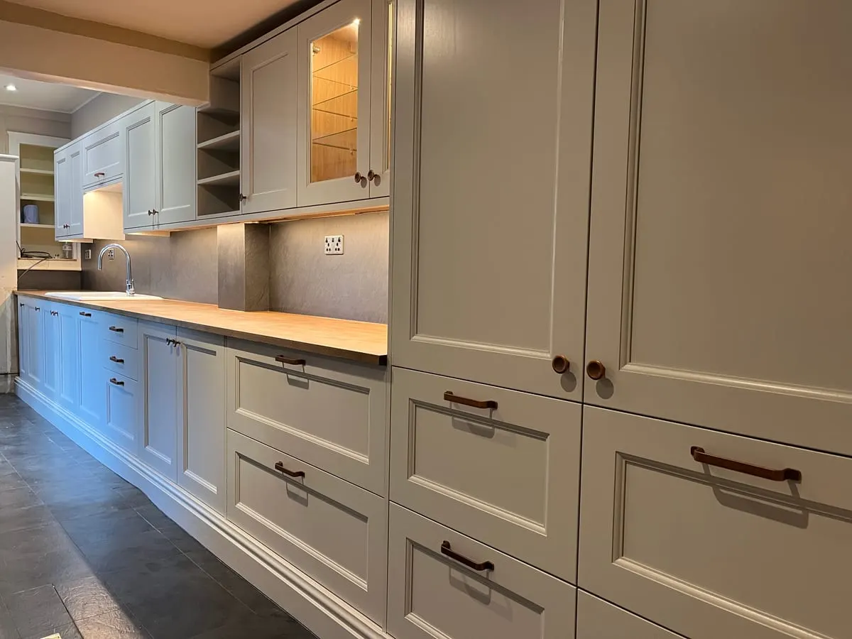 Painted in-frame kitchen run with oak worktop, tall larder units, leather pull handles and slate floor