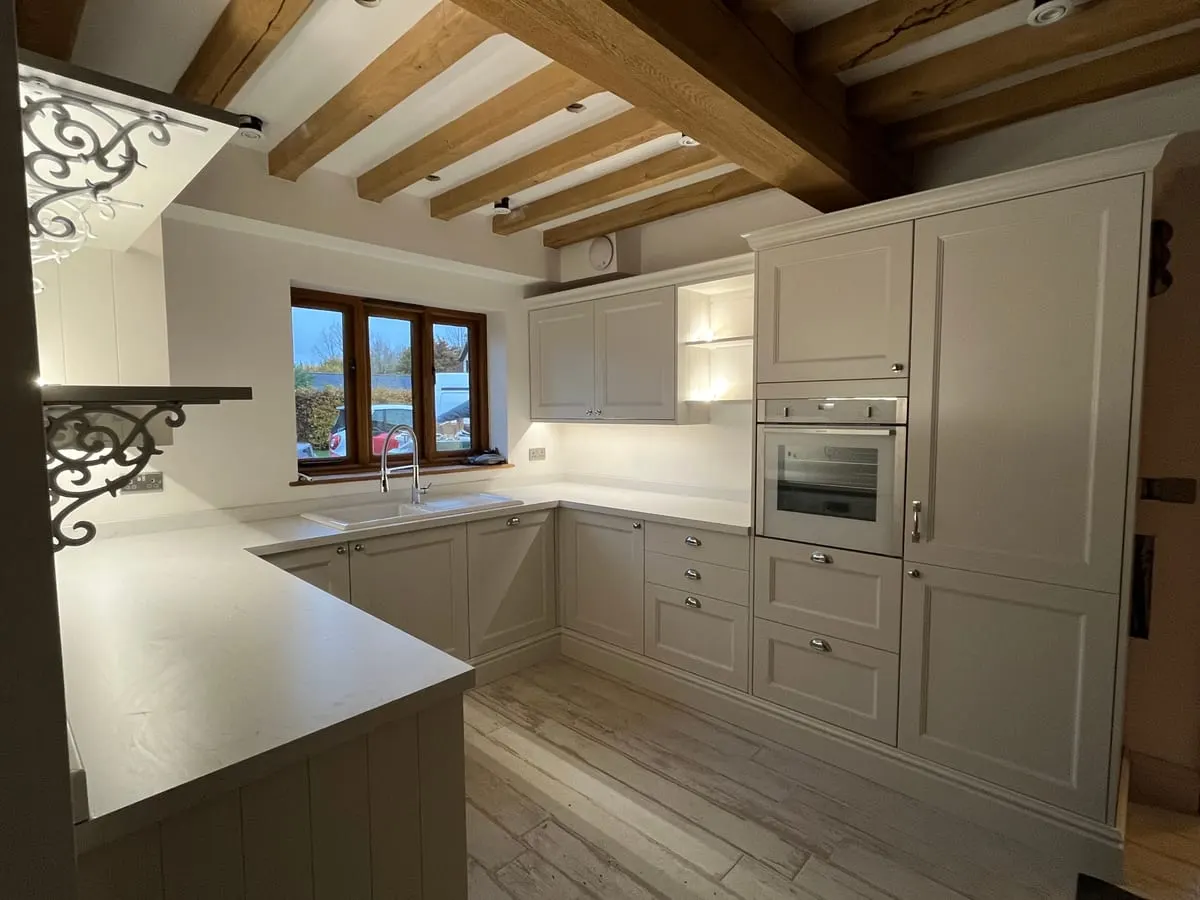 Cream shaker kitchen with peninsula, quartz worktops and built-in oven below exposed oak beams