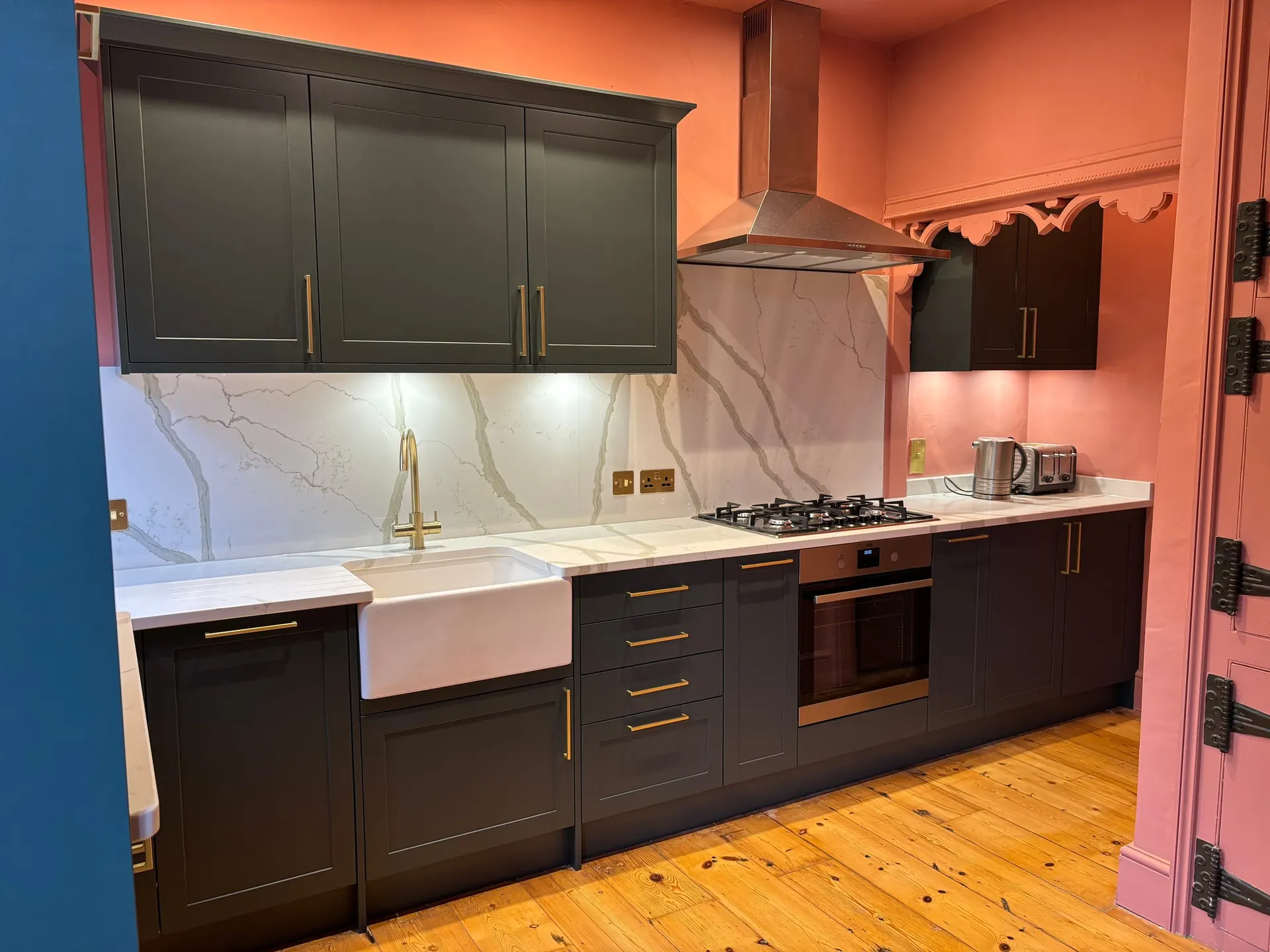Dark shaker kitchen with marble splashback, brass handles, butler sink and stainless steel extractor hood