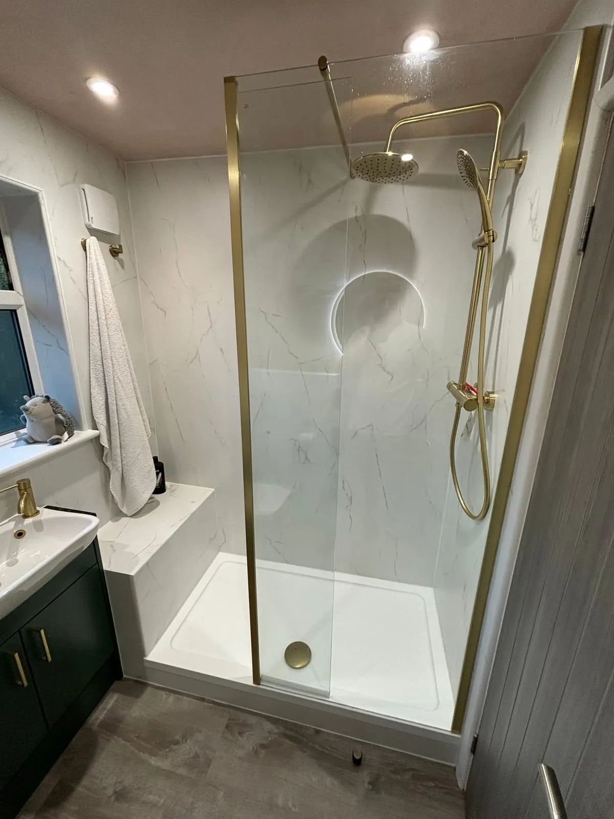 Walk-in shower with brushed brass rainfall fittings, marble-effect panels and built-in seat