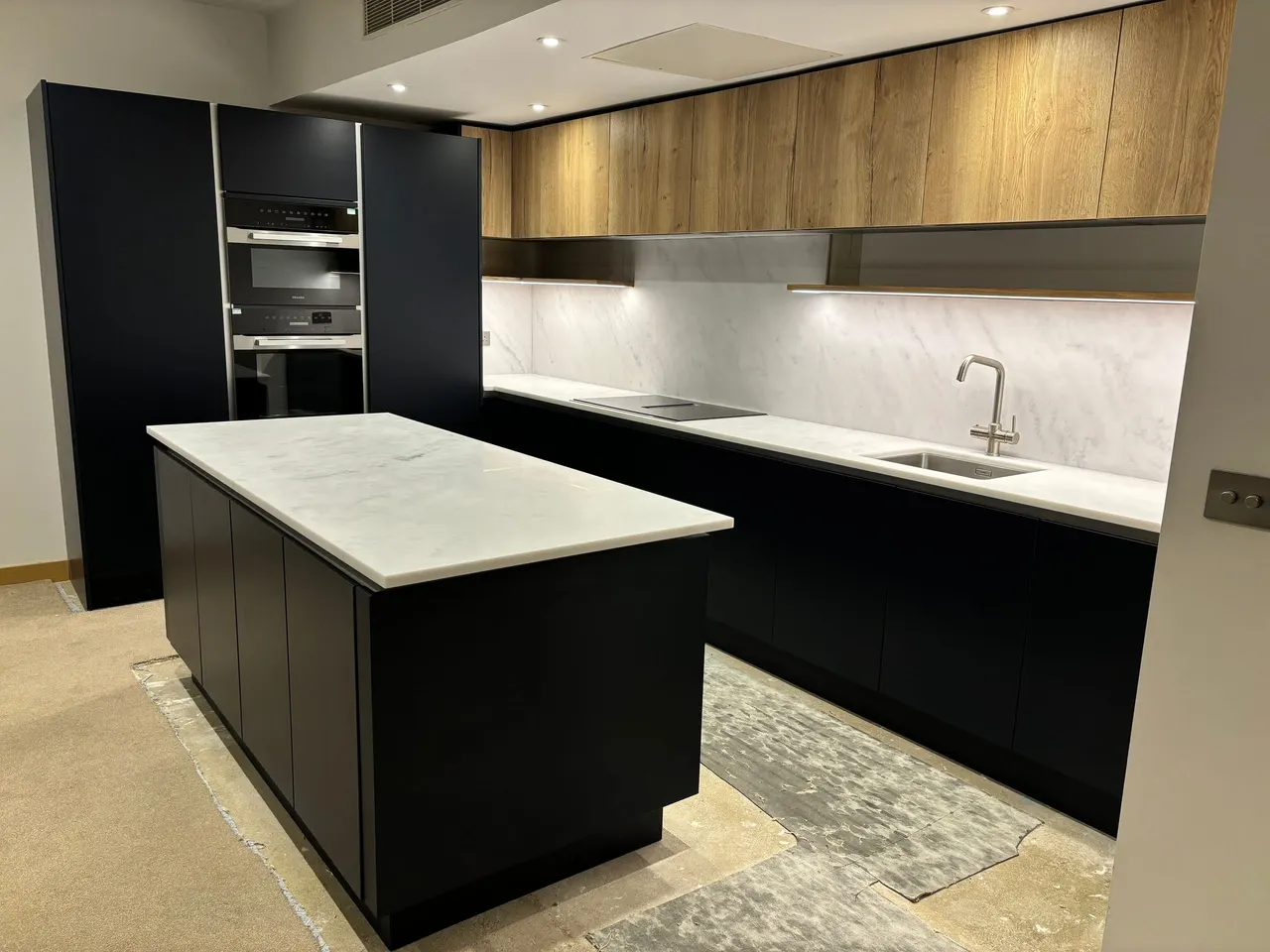 Handleless matt black kitchen with marble-topped island, oak wall units and integrated ovens